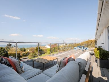 An outdoor terrace with a sofa and coffee table overlooking a garden and distant sea at Atlanta near Tintagel