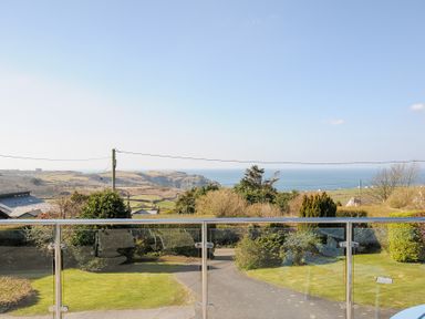 A view of a coastal landscape with grass and bushes seen from behind a glass balcony railing at Atlanta near Tintagel