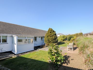 A garden with a bench a bush and a white house near Tintagel