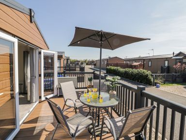 A balcony with a round glass table, four chairs, an umbrella, and drinks at Casa De Rhu in Evesham