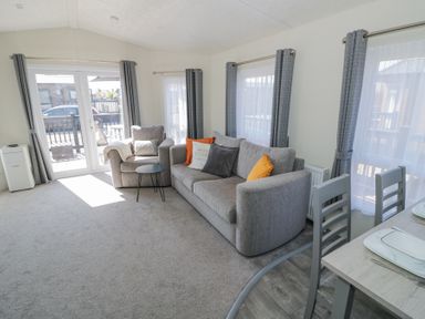 A living room with a gray sofa and armchair with cushions a small round table and dining table with chairs at Casa De Rhu in Evesham