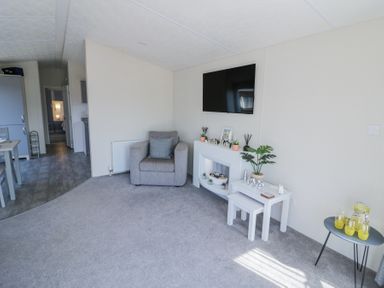 A living room with a gray armchair a wall mounted television a small white table with stools and a folding table with drinks at Casa De Rhu in Evesham
