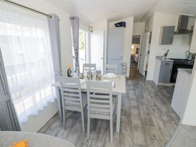 A dining area with a set table and gray chairs next to large windows and a kitchen in Casa De Rhu in Evesham