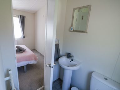 A small bathroom with a sink toilet and mirror and a bedroom with a bed and window at Casa De Rhu in Evesham