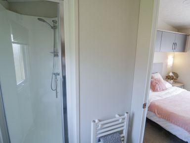 A bathroom with a shower next to a bedroom with a bed and overhead cabinets at Casa De Rhu in Evesham