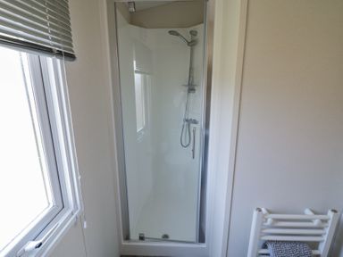 A bathroom with a glass door shower enclosure a shower head window with blinds and a towel rack at Casa De Rhu in Evesham