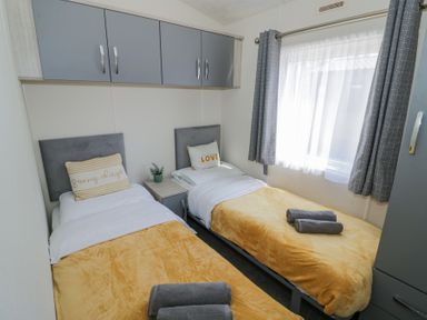 A bedroom with two single beds with yellow blankets and pillows under gray cabinets at Casa De Rhu in Evesham