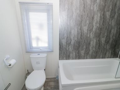 A bathroom with a toilet next to a bathtub and a window with blinds at Casa De Rhu in Evesham