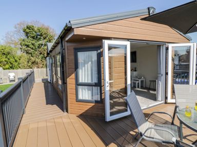 A wooden deck with metal chairs and table outside a building with open glass doors at Casa De Rhu in Evesham