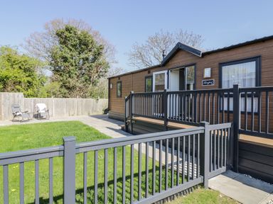 A fenced yard with grass and two chairs outside a wooden cabin at Casa De Rhu in Evesham