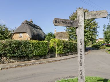 A rural street with a wooden signpost showing directions to Cotswold Way and Surgery with thatched cottages and hedges in the background at Casa De Rhu in Evesham