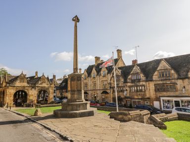 A town square with a stone monument a flagpole with a union jack and historic stone buildings in the background at Casa De Rhu in Evesham