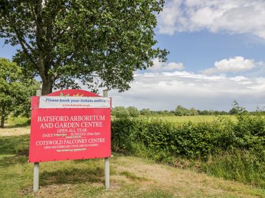 A sign for Batsford Arboretum and Garden Centre near a tree and grassland at Casa De Rhu in Evesham
