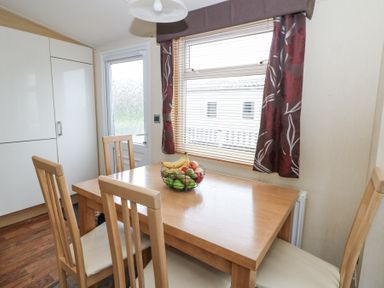 A dining area with a wooden table and four chairs with a fruit basket on the table and a window with floral curtains at 21 Bay View in Maenygroes near New Quay Ceredigion