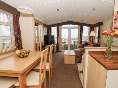 A living room and dining area with wooden table chairs fruit bowl sofa coffee table and television at 21 Bay View in Maenygroes near New Quay Ceredigion