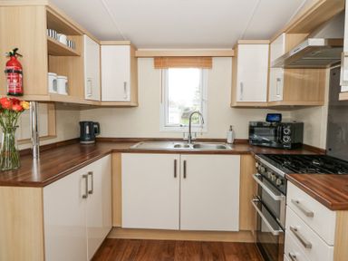 A kitchen with wooden countertops white cabinets a gas stove a black microwave a sink under a window and a vase of flowers on the counter at 21 Bay View Maenygroes near New Quay Ceredigion