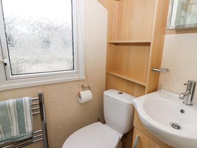 A bathroom with a toilet sink wooden shelves frosted window and a towel rack at 21 Bay View in Maenygroes near New Quay Ceredigion
