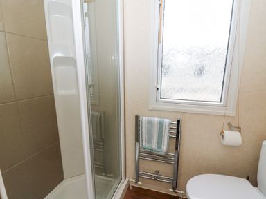 A bathroom with a shower enclosure a towel rail with a towel a frosted window and a toilet at 21 Bay View in Maenygroes near New Quay Ceredigion