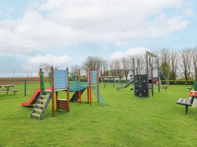 A playground with slides climbing structures and benches on grass at 21 Bay View in Maenygroes near New Quay Ceredigion