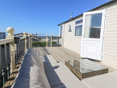 An outdoor deck area with a sofa and glass coffee table outside a beige building at 21 Bay View in Maenygroes near New Quay Ceredigion
