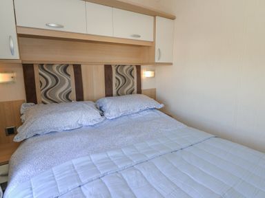 A bedroom with a double bed with light blue bedding and patterned headboard with overhead storage cabinets at 21 Bay View in Maenygroes near New Quay Ceredigion