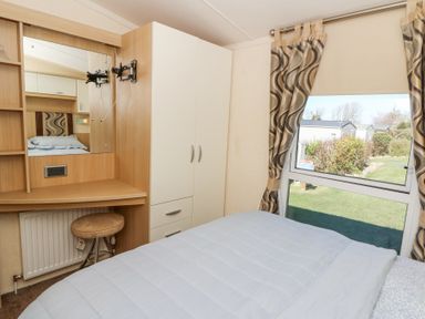 A bedroom with a bed white wardrobe dressing table and window with patterned curtains at 21 Bay View Maenygroes near New Quay Ceredigion
