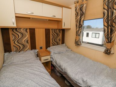 A small bedroom with two single beds side by side a nightstand in between and a window with patterned curtains at 21 Bay View Maenygroes near New Quay Ceredigion