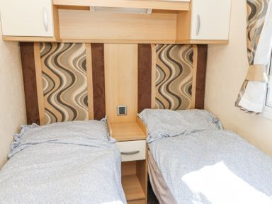 A bedroom with two single beds separated by a small wooden nightstand under a wooden cabinet at 21 Bay View in Maenygroes near New Quay Ceredigion