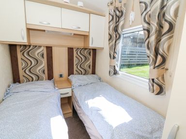 A bedroom with two single beds a window and overhead cabinets at 21 Bay View in Maenygroes near New Quay Ceredigion