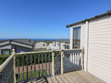 An outdoor deck with a wooden railing and gate overlooking a cluster of beige mobile homes with the sea in the background at 21 Bay View in Maenygroes near New Quay Ceredigion