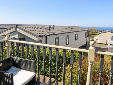 A balcony with a wicker chair overlooking a row of mobile homes and the sea at 21 Bay View in Maenygroes near New Quay Ceredigion