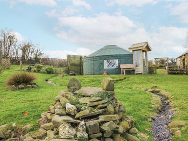 A garden with stone landscaping a small stream a circular tent and wooden bench at Blaidd Bach in Carmarthen