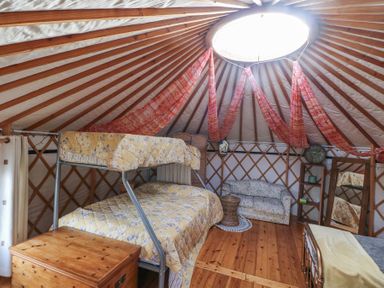 An interior of a yurt with a bunk bed mattress a sofa a wooden chest a small table and a standing mirror at Blaidd Bach in Carmarthen