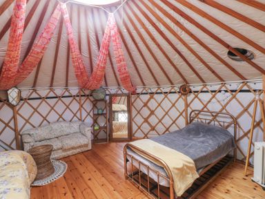 A room inside a yurt with a metal bed frame a couch a mirror and wooden floor at Blaidd Bach in Carmarthen