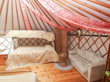 An interior of a yurt with a bunk bed covered with yellow floral quilts a floral sofa a wicker table and wooden flooring at Blaidd Bach in Carmarthen
