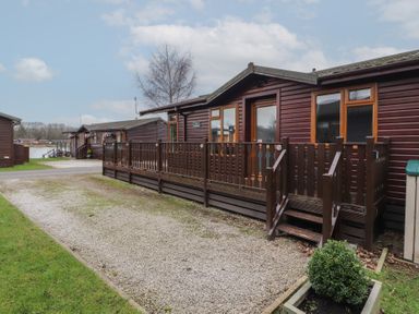 A wooden cabin with a fenced porch and gravel driveway near water at Lakeside 18 in Carnforth