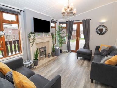 A living room with sofas a fireplace plants and a television at Lakeside 18 in Carnforth