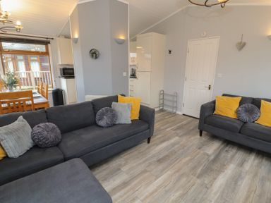 A living room with two dark sofas with cushions and a wooden dining table with chairs near a window at Lakeside 18 in Carnforth