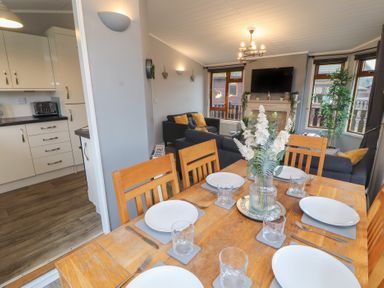 A dining table set with plates and glasses adjacent to a living room with sofas and a wall-mounted TV at Lakeside 18 Carnforth