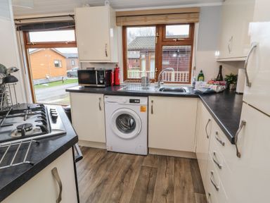 A kitchen with a washing machine sink microwave and gas stove at Lakeside 18 in Carnforth