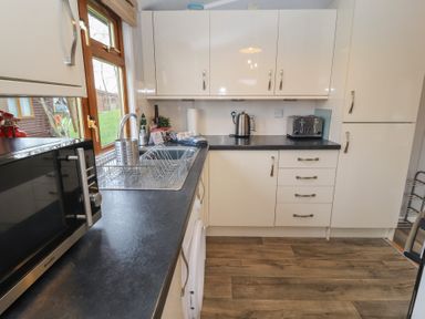 A kitchen with black countertops white cabinets a microwave a kettle a toaster and a window showing an outside view at Lakeside 18 in Carnforth
