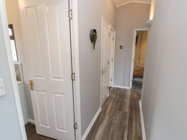 A hallway with wooden floor and white doors leading to different rooms at Lakeside 18 in Carnforth
