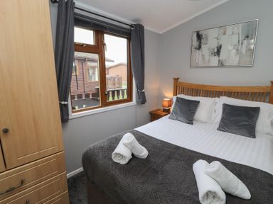 A bedroom with a wooden bed frame gray pillows white rolled towels and a wooden wardrobe at Lakeside 18 Carnforth