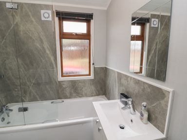 A bathroom with a bathtub shower combo a window above the bathtub and a sink with a mirror above it at Lakeside 18 in Carnforth