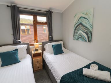 A bedroom with two single beds separated by a wooden nightstand with a lamp and remote controls at Lakeside 18 in Carnforth