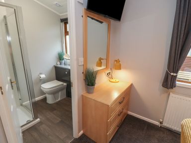 A bathroom with a toilet and shower and a room with a wooden chest of drawers a mirror and a lamp at Lakeside 18 in Carnforth