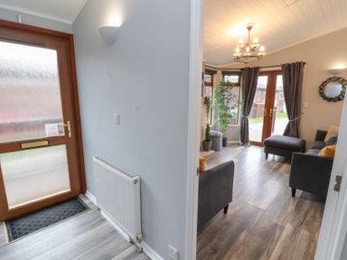 An entrance area with a radiator and a door leading to a living room with sofas plants and a chandelier at Lakeside 18 in Carnforth