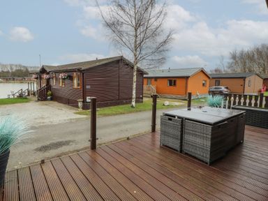 A wooden deck with outdoor furniture and a view of wooden lodges near a lake at Lakeside 18 in Carnforth
