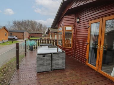 A wooden deck with outdoor furniture and railings outside a wooden cabin at Lakeside 18 in Carnforth
