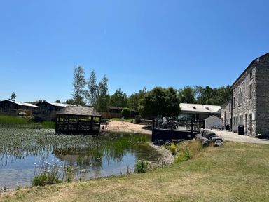 A lakeside area with a wooden gazebo on the water and stone buildings with people sitting on the patio at Lakeside 18 in Carnforth
